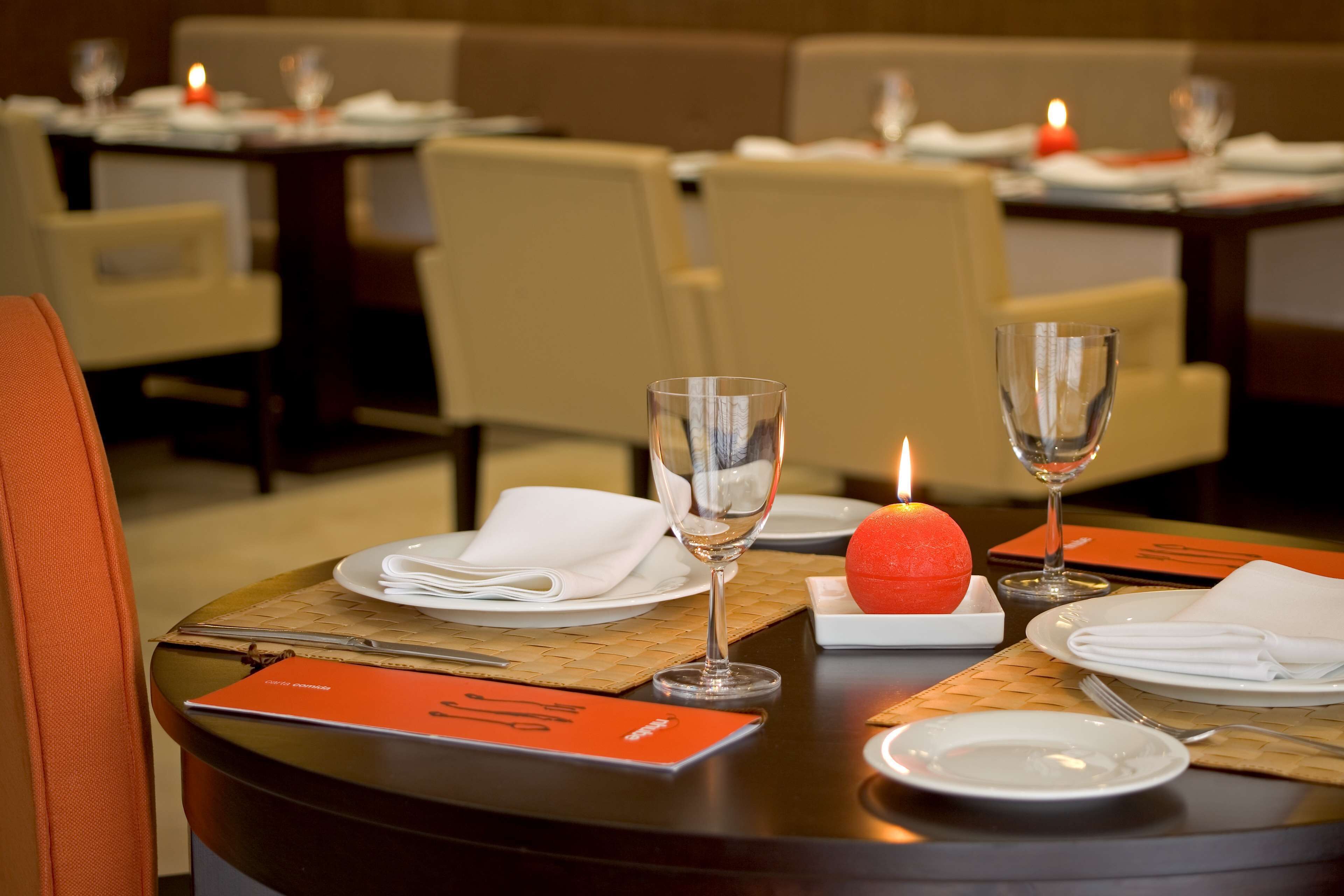 Una mesa de comedor dispuesta con platos, vasos y una vela, en un restaurante con sillas acolchadas.