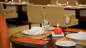 Una mesa de comedor dispuesta con platos, vasos y una vela, en un restaurante con sillas acolchadas.