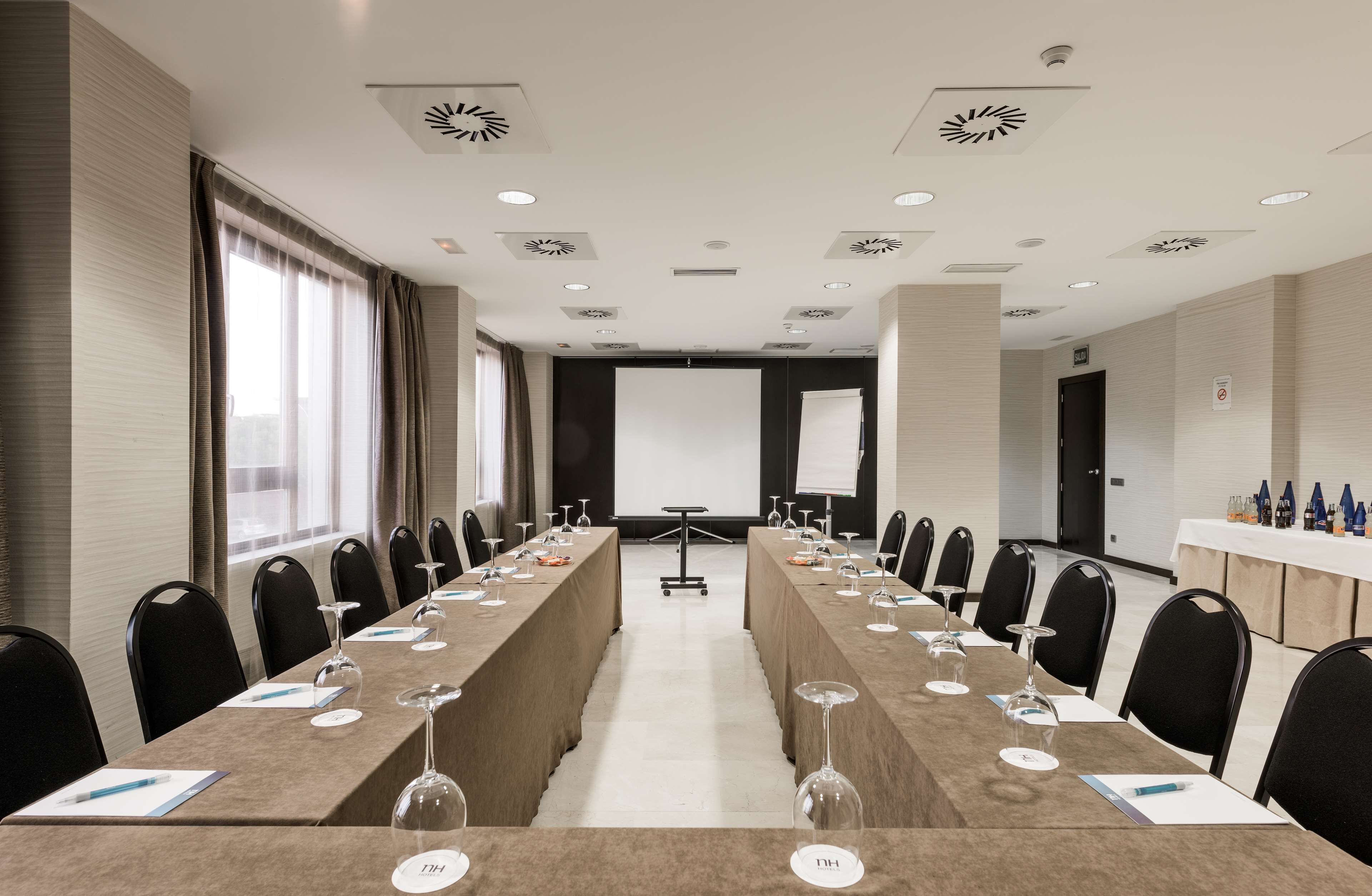 Un salón de conferencias con una larga mesa, sillas, una pantalla de proyector y una pizarra.