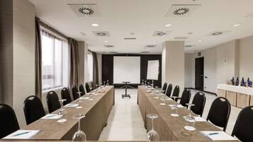 Un salón de conferencias con una larga mesa, sillas, una pantalla de proyector y una pizarra.