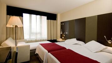 A hotel room with two beds, a desk, a lamp, and a nightstand.