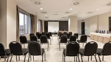 A conference room with rows of black chairs facing a long table with a projector screen at the front.