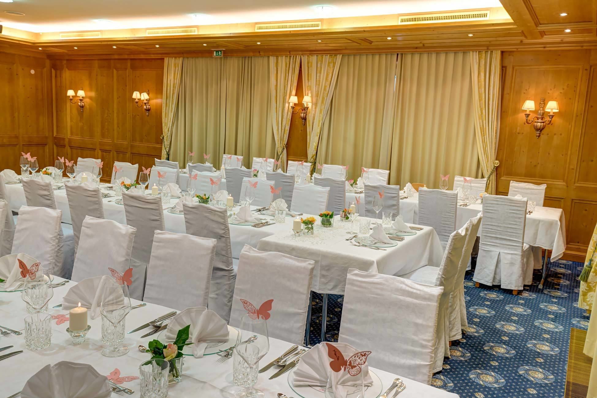 A banquet hall with multiple round tables set for dining, white tablecloths, and chairs with white covers.