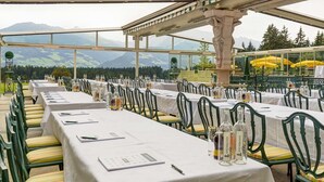 Zona de comedor al aire libre con mesas dispuestas para una comida, con vistas a un paisaje montañoso.