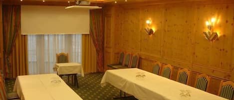 A conference room with a long table, chairs, a projector screen, and wall-mounted lamps.