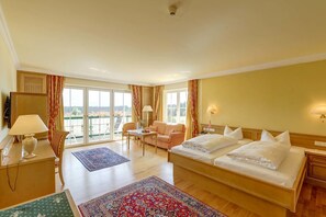 A hotel room with a large bed, a sofa, a desk with a lamp, and a view of the outdoors through the windows. - Alpenhotel Speckbacher Hof (Gnadenwald)