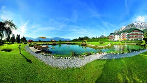 Un hotel con un estanque grande, césped verde y montañas al fondo.
