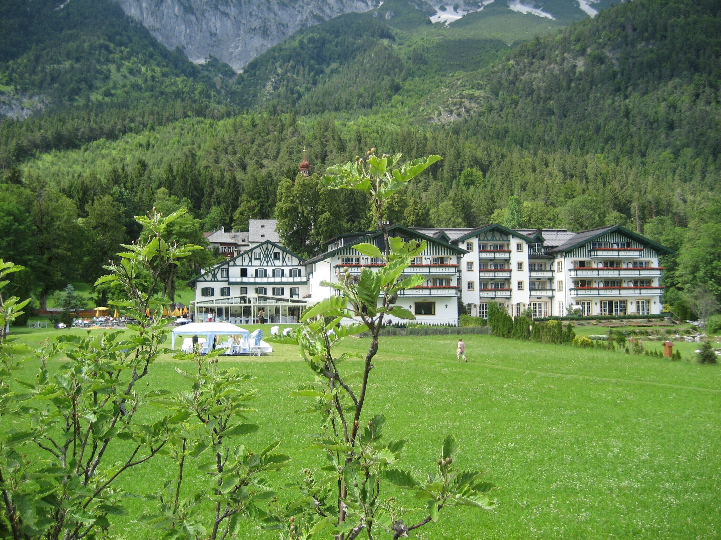 Un grand hôtel à étages multiples, doté de balcons et entouré d’une végétation luxuriante et de montagnes.