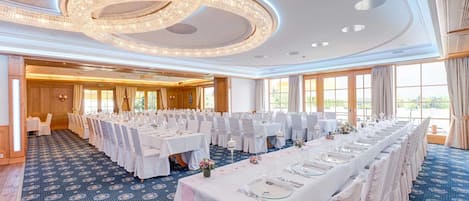 A banquet hall with round tables, white tablecloths, and chairs.