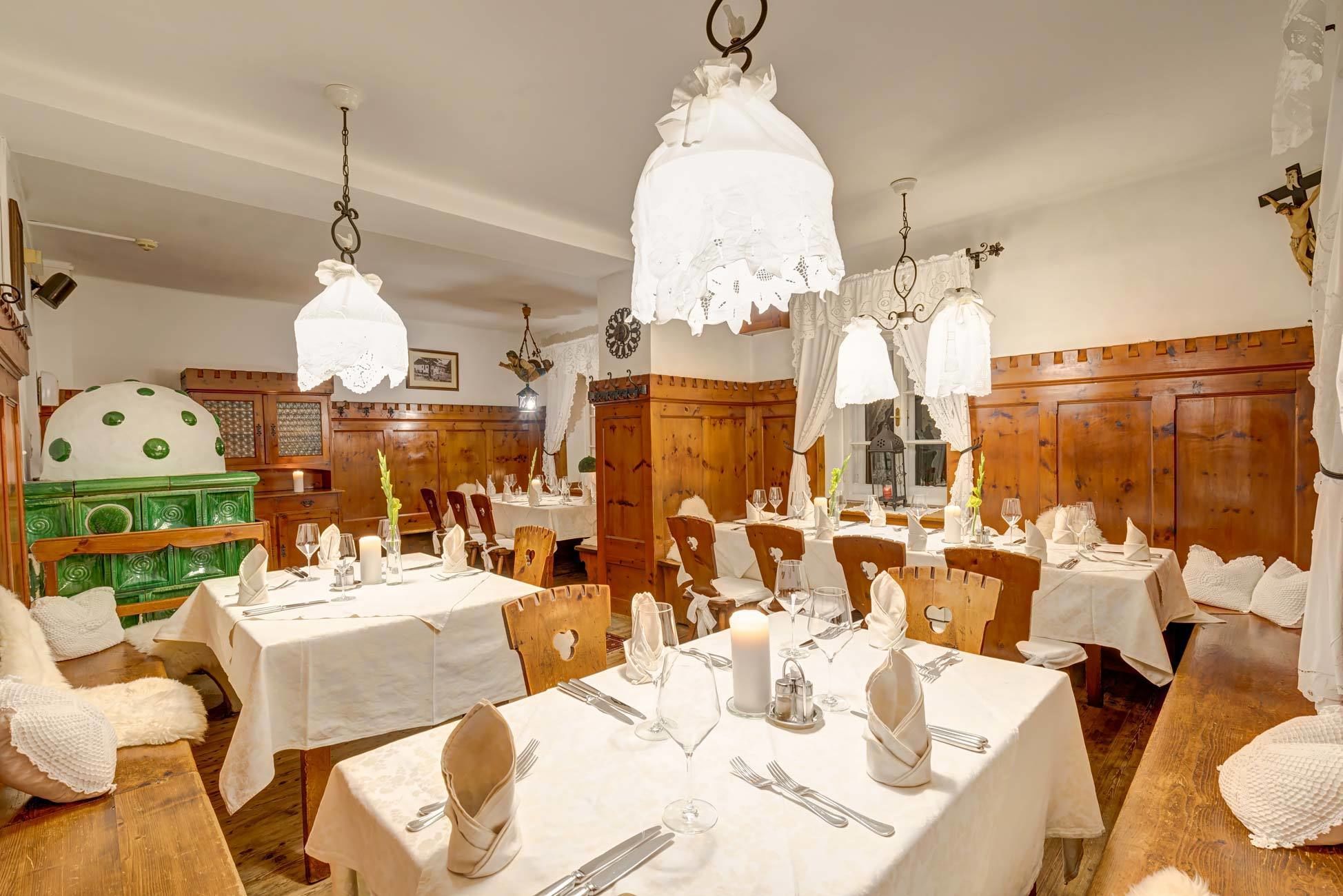 A restaurant with multiple tables set for dining, wooden paneling on the walls, and hanging white lamps.