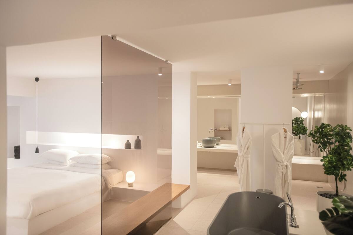 A modern hotel room with a bed, bedside table, nightstand, and a large mirror.