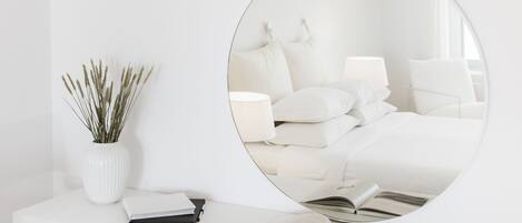 A white bedside table with a mirror, a white vase with dried plants, and a book.