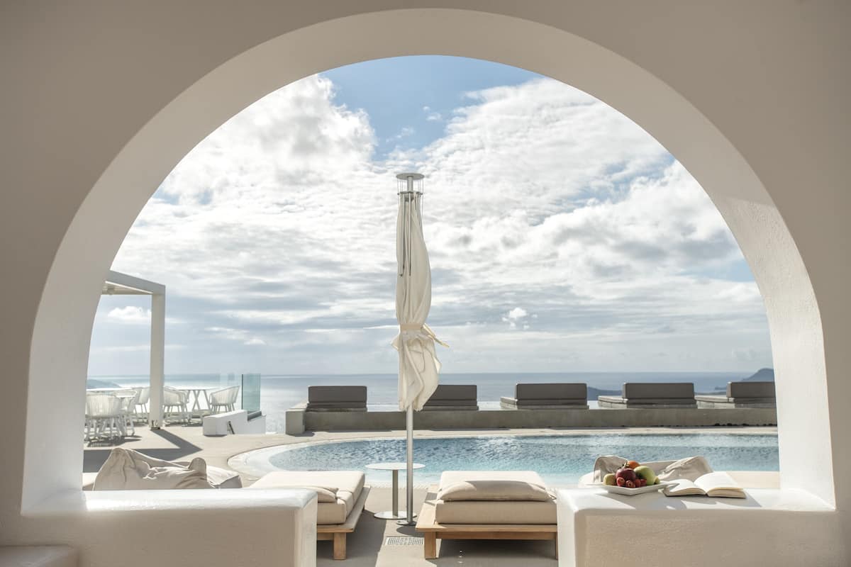 A poolside area with lounge chairs and an umbrella, overlooking a body of water and a clear sky.