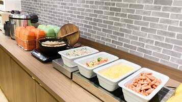 A buffet line with various food containers, a kettle, and stacked plates.