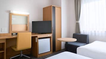A hotel room with a bed, a desk with a chair, a television, a minibar, and a small round table.