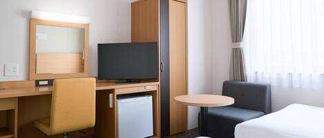 A hotel room with a bed, a desk with a chair, a television, a minibar, and a small round table.