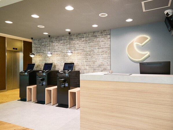 A reception area with a brick wall, three computer kiosks, a reception desk, and a large illuminated arrow sign.
