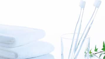 A stack of white towels, a glass with two toothbrushes, and a green plant.