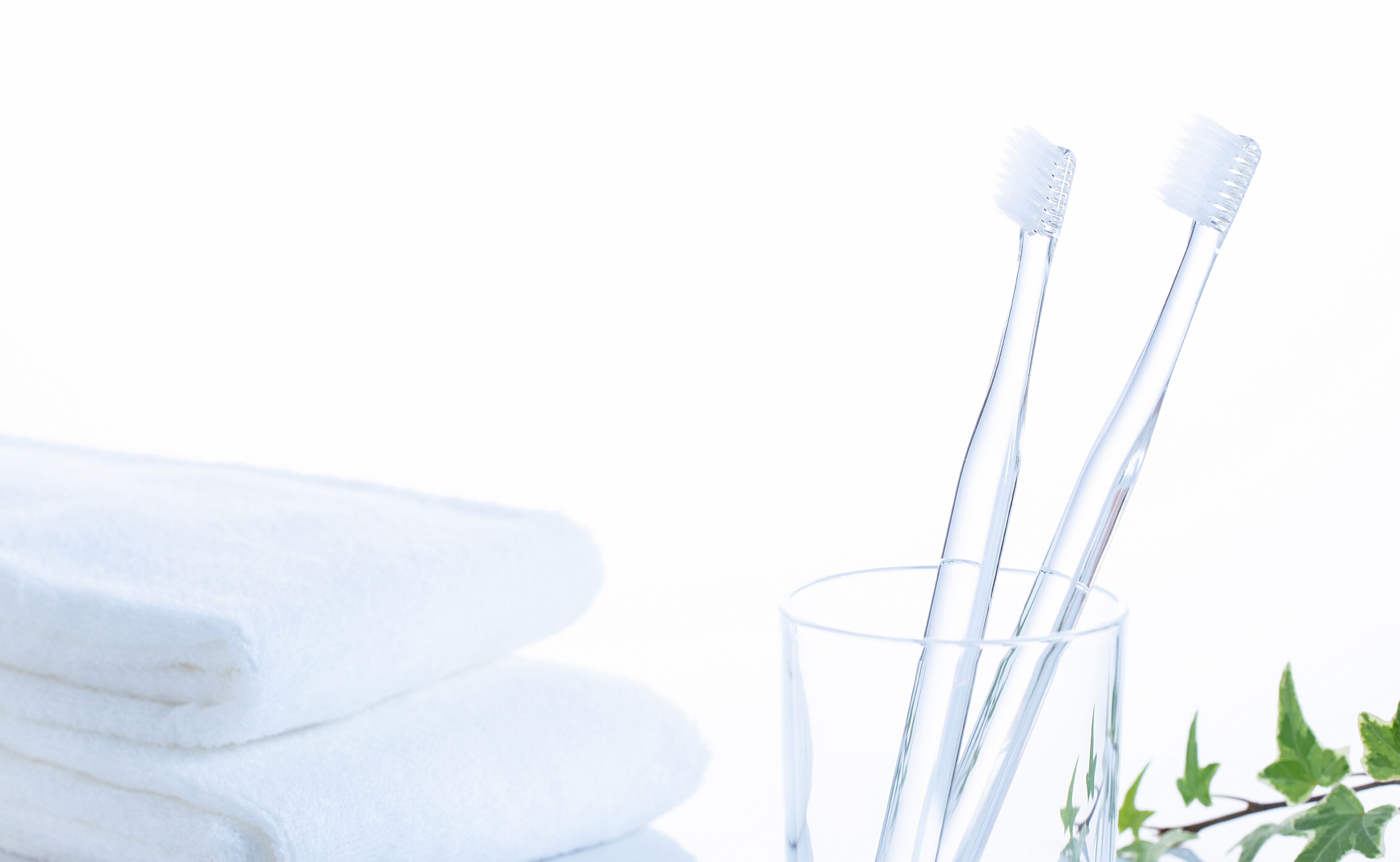 A stack of white towels and two toothbrushes in a clear glass.