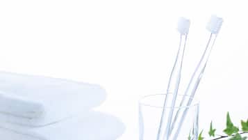 Una pila de toallas blancas y dos cepillos de dientes en un vaso transparente.