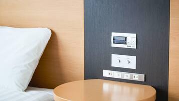Une chambre d’hôtel comprenant un lit, une table de chevet, une horloge numérique et un panneau de commande avec des boutons pour régler l’inclinaison du lit et du repose-pieds.