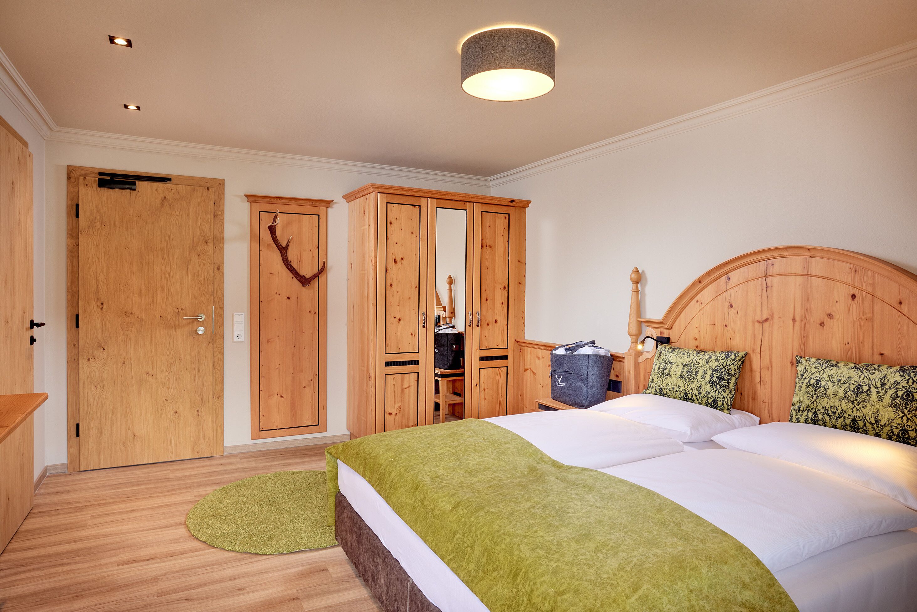 A bedroom with a wooden wardrobe, a bed with green bedding, and a headboard.