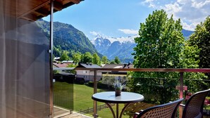 A balcony with a wooden floor, a round table, and two chairs. A potted plant is on the table. - Hotel Sonnblick (Kaprun)