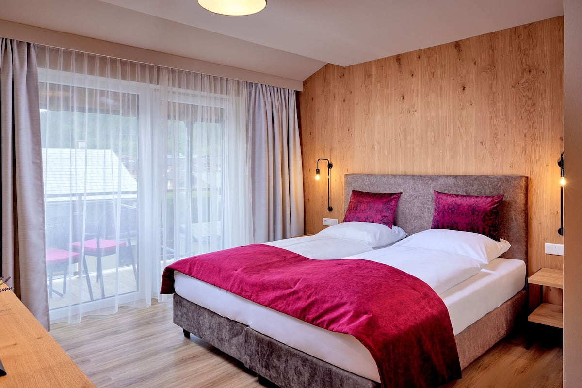 A double bed with a red blanket, wooden headboard, and two bedside lamps.