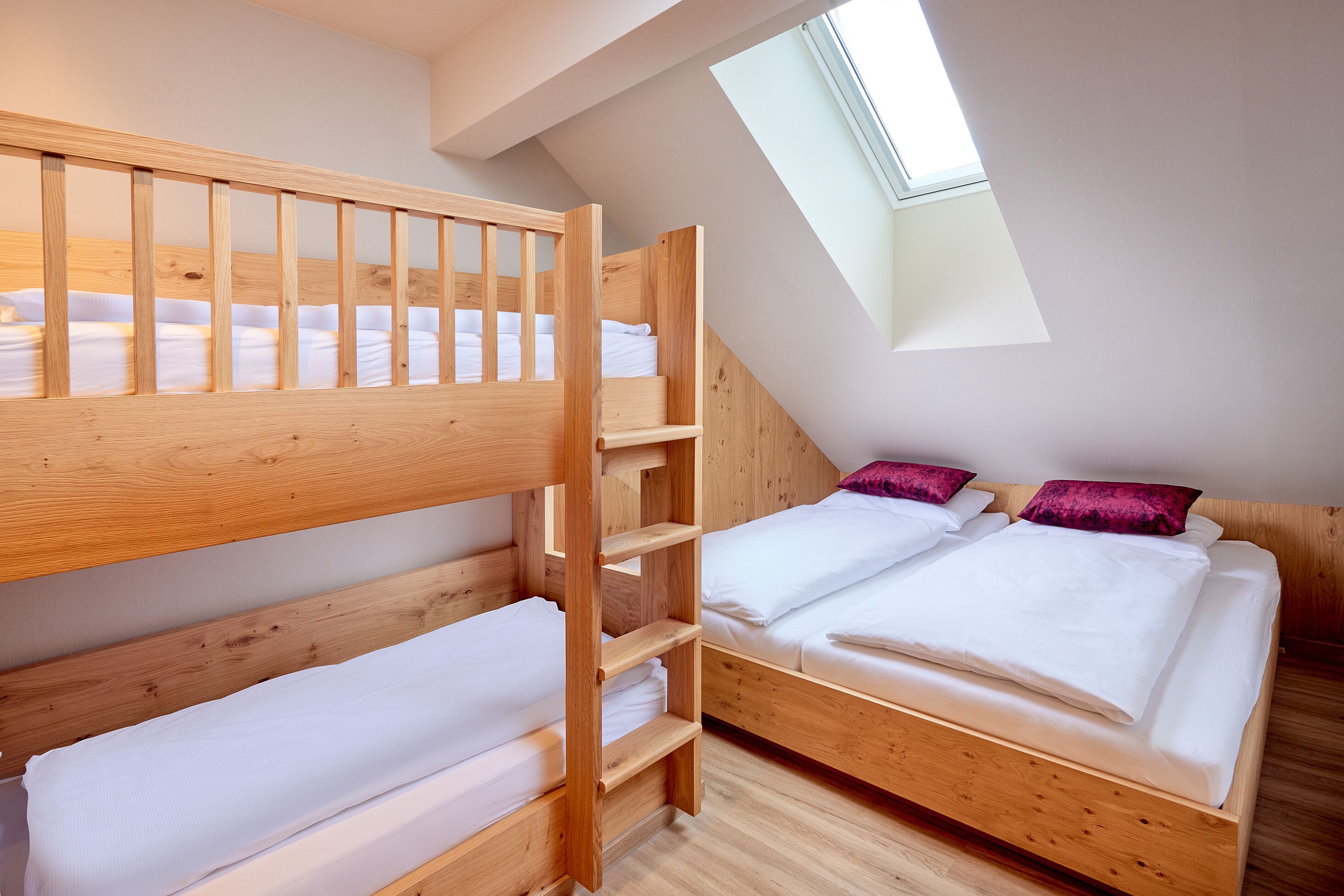 A dorm-style room with bunk beds, a skylight, and a wooden floor.
