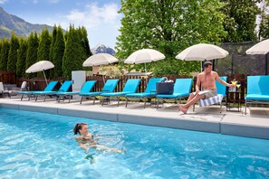 A swimming pool with lounge chairs and umbrellas, a wooden fence, and a mountain backdrop. - Hotel Sonnblick (Kaprun)