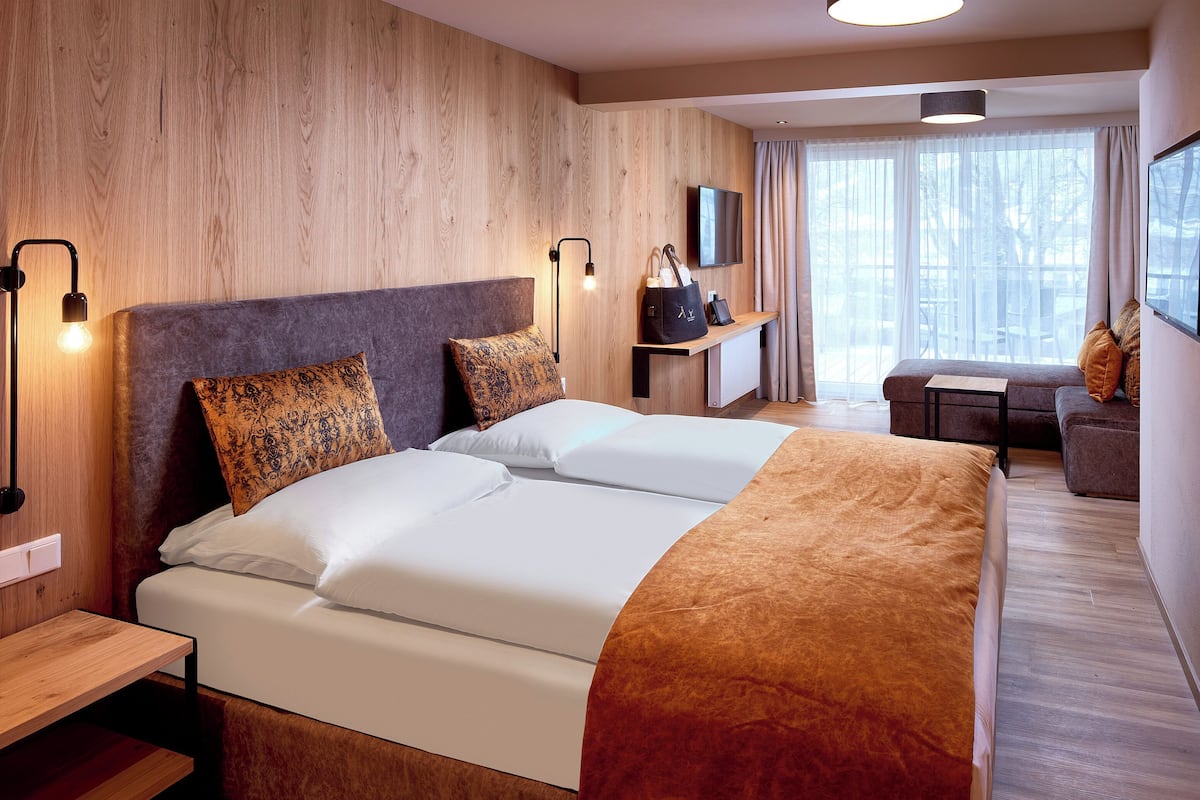 A hotel room with two beds, a TV, a desk, and a window with curtains.