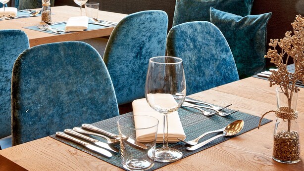 A dining area with a table set for two, a window with a mountain view, and a cozy seating arrangement. - Hotel Sonnblick (Kaprun)