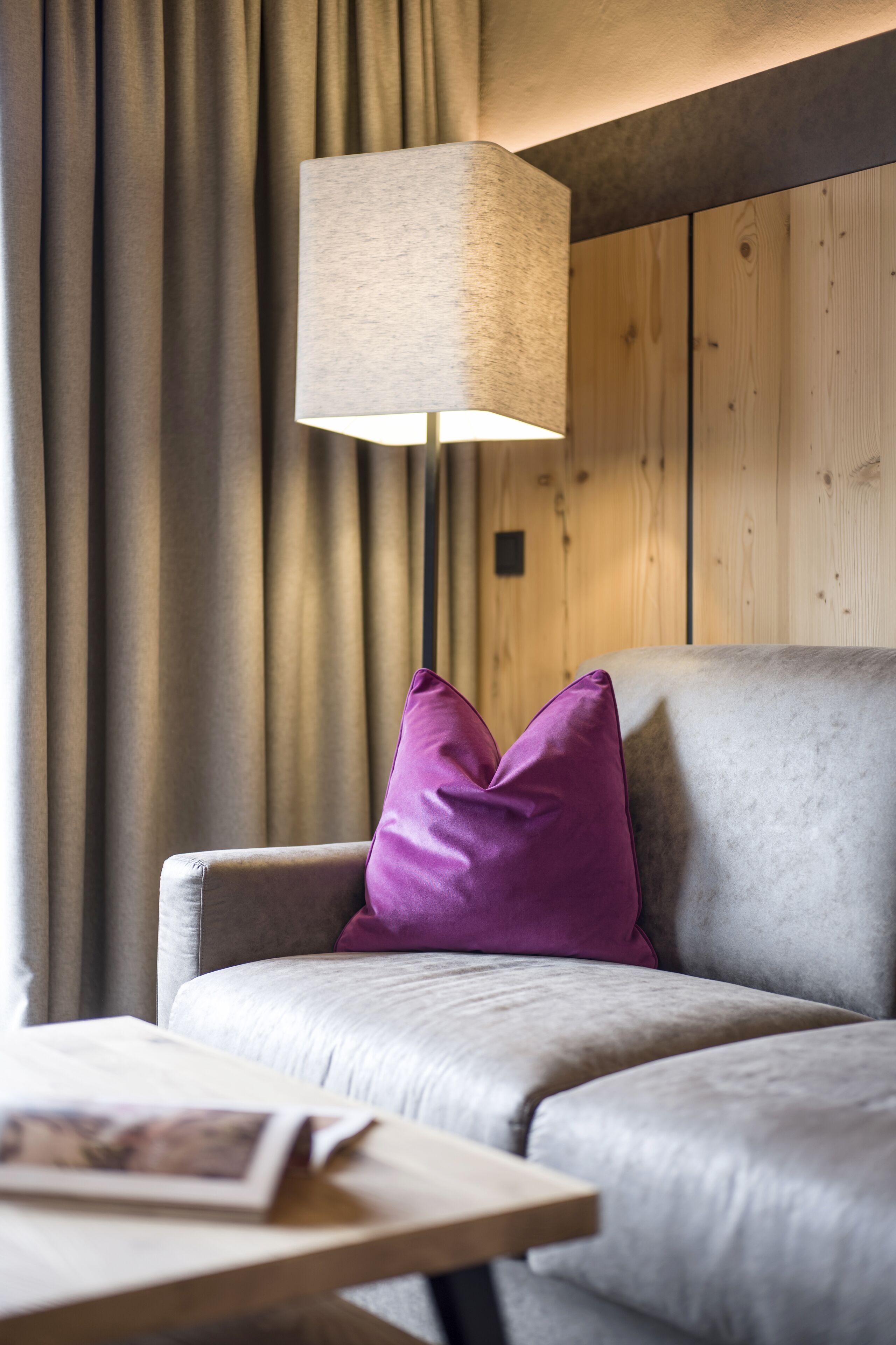 A sofa with a cushion, a lamp, a table, and curtains.