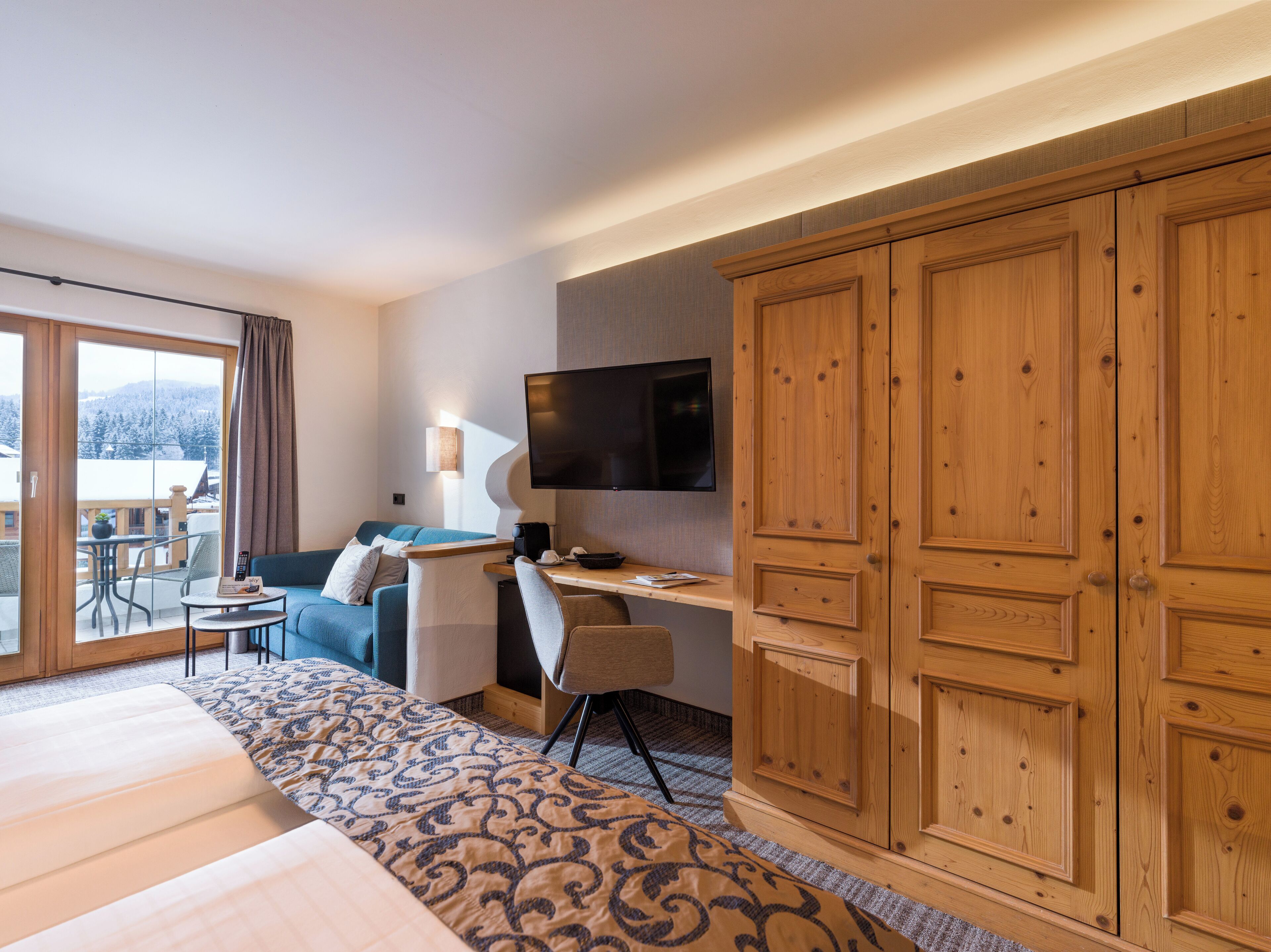 A hotel room with a bed, a desk, a chair, a TV, and a wardrobe.