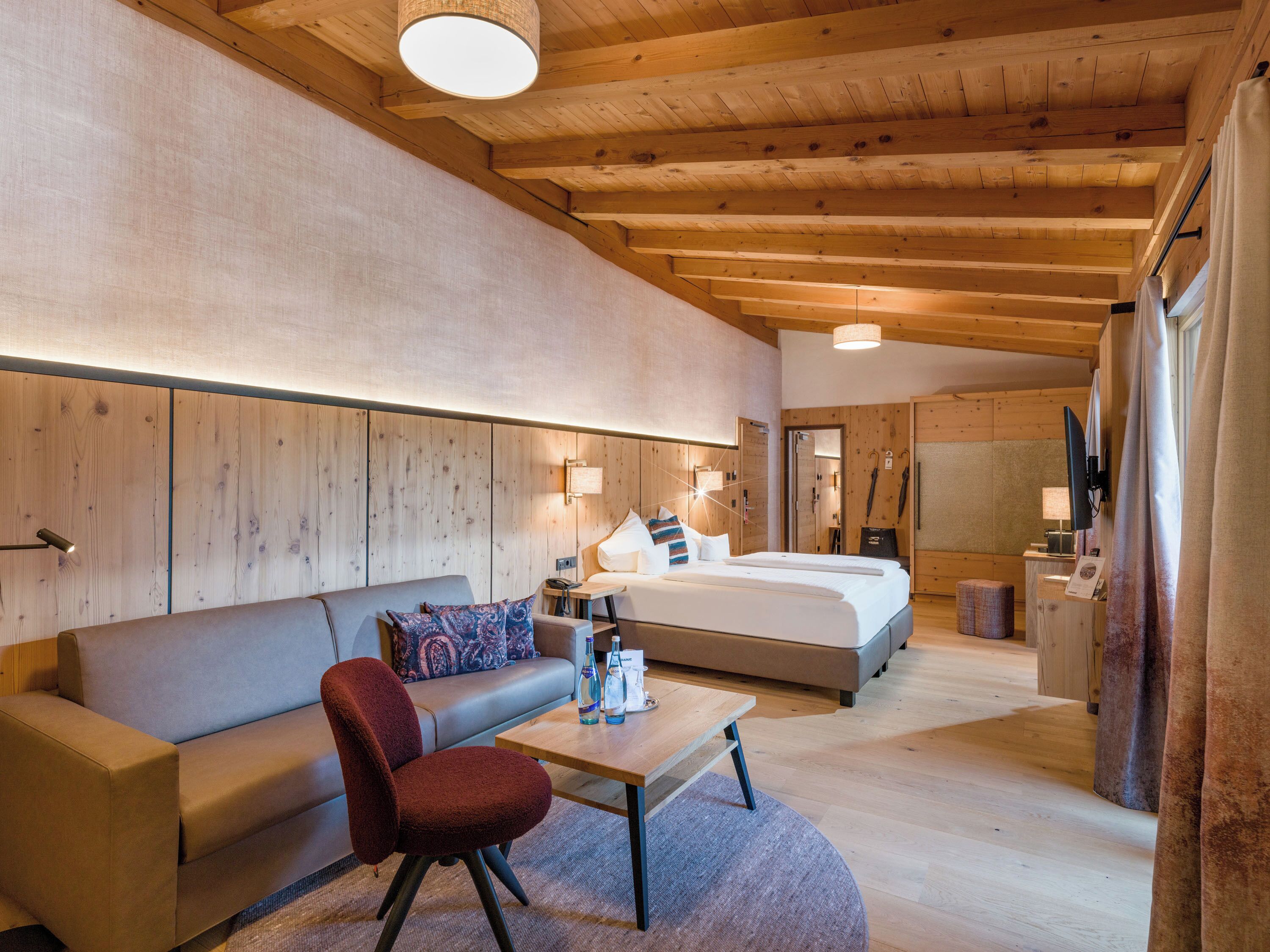 Ein modernes Hotelzimmer mit Holzboden, einem Bett, einem Sofa, einem Sessel und einem kleinen Tisch.