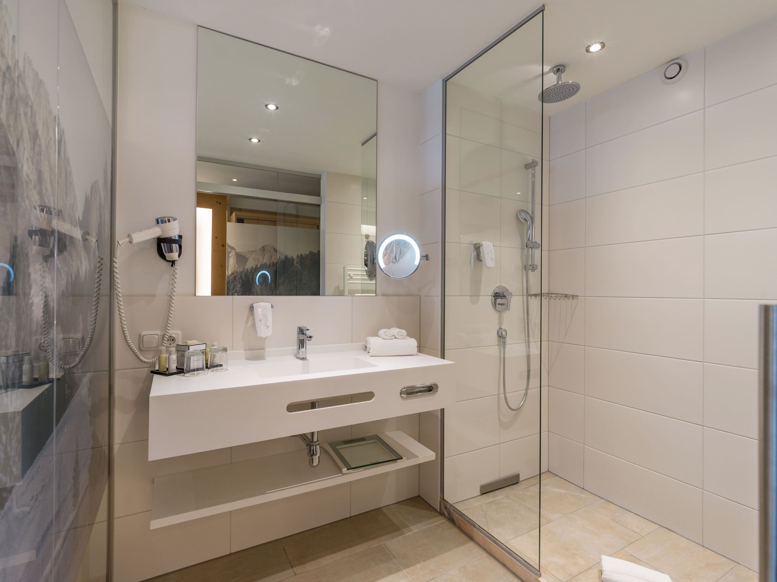 Une salle de bain moderne avec une douche à parois de verre, un meuble-lavabo blanc avec un miroir et un sèche-cheveux fixé au mur.