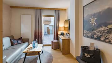 Et moderne hotelværelse med en sofa, et træ sofabord, et skrivebord med lampe, et stort maleri og udsigt til udeområdet.