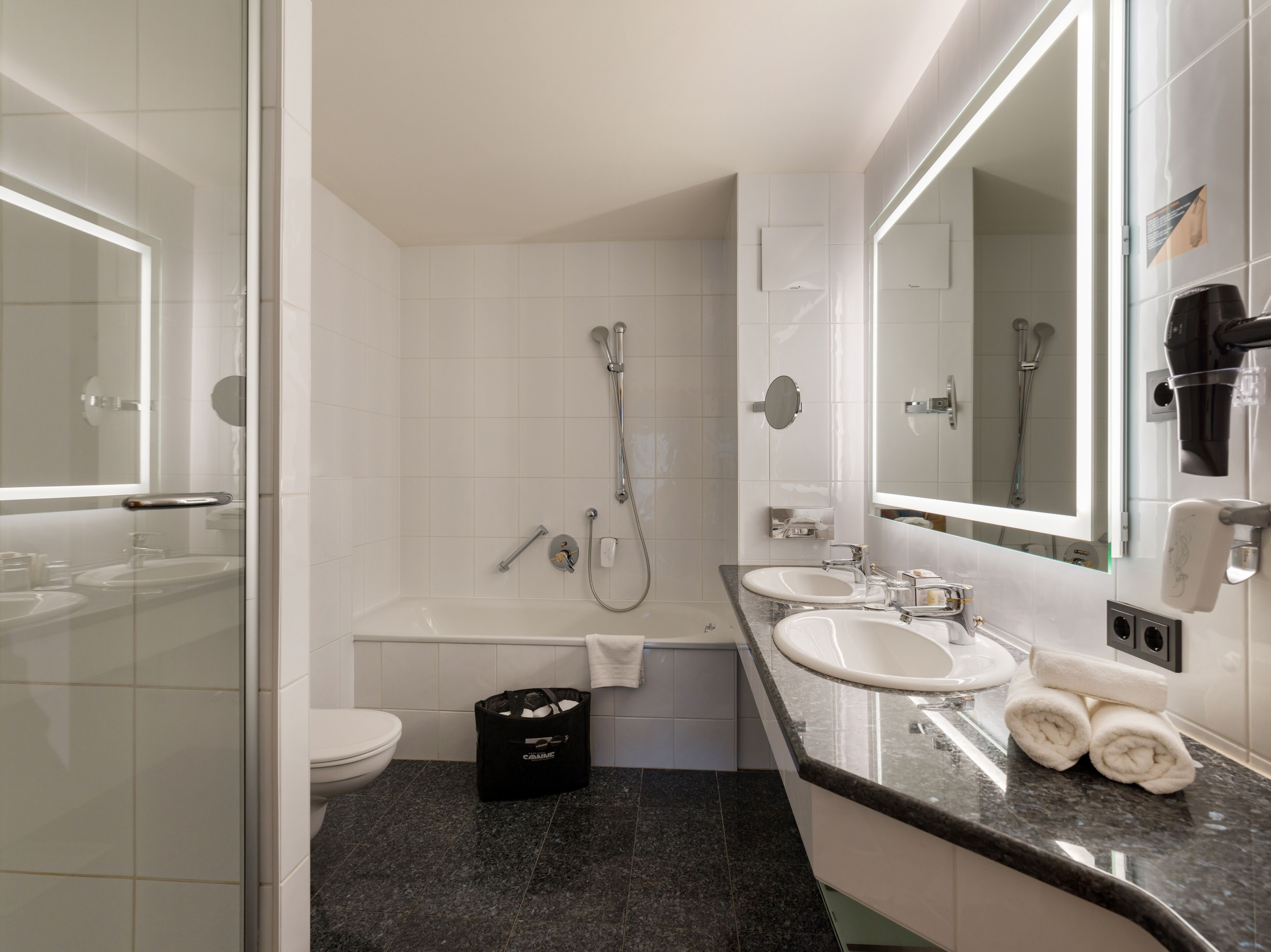 A modern bathroom with a glass shower enclosure, a bathtub, two sinks, and a large mirror.
