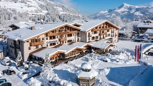 A snow-covered mountain resort with wooden buildings and a ski slope in the background. -  Hotel Sonne 4 Sterne Superior (Kirchberg in Tirol)