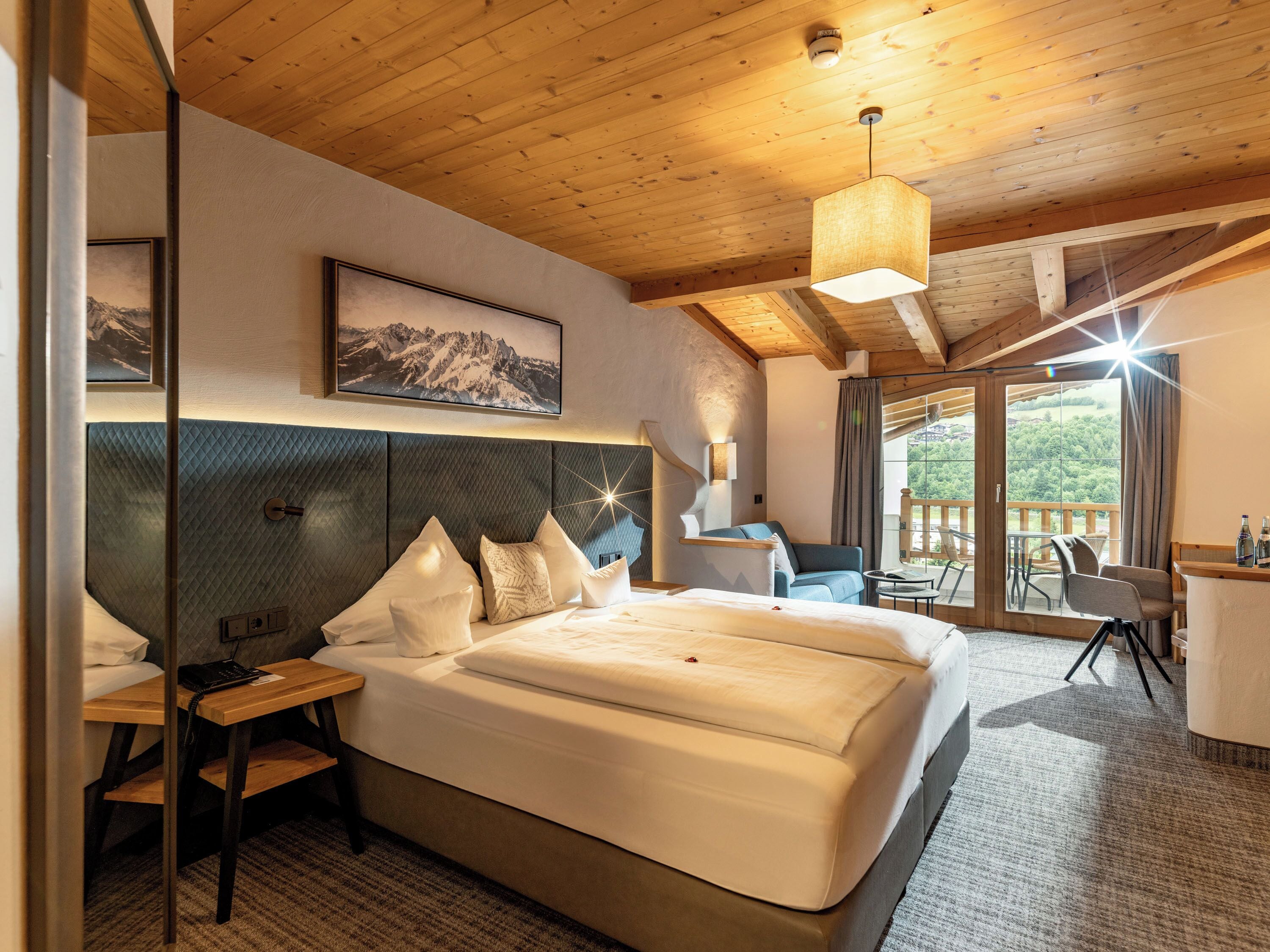 A modern hotel room with a large bed, a desk, a chair, and a view of the outdoors.