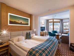 A hotel room with a large bed, a desk with a TV, a chair, and a view of the mountains through the window.