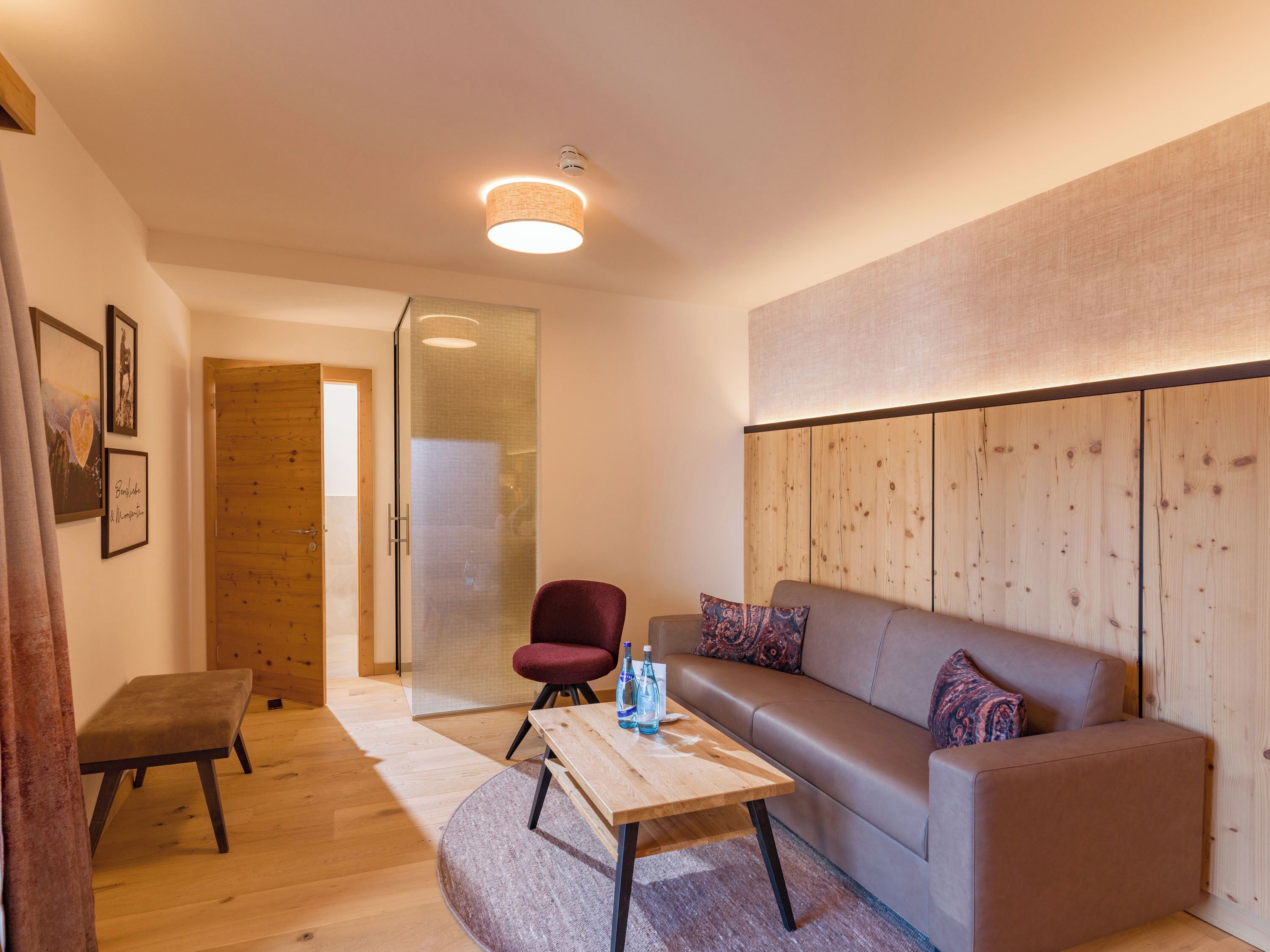 Una sala moderna con un sofá, un banco de madera, una puerta de vidrio y un panel de pared de madera.