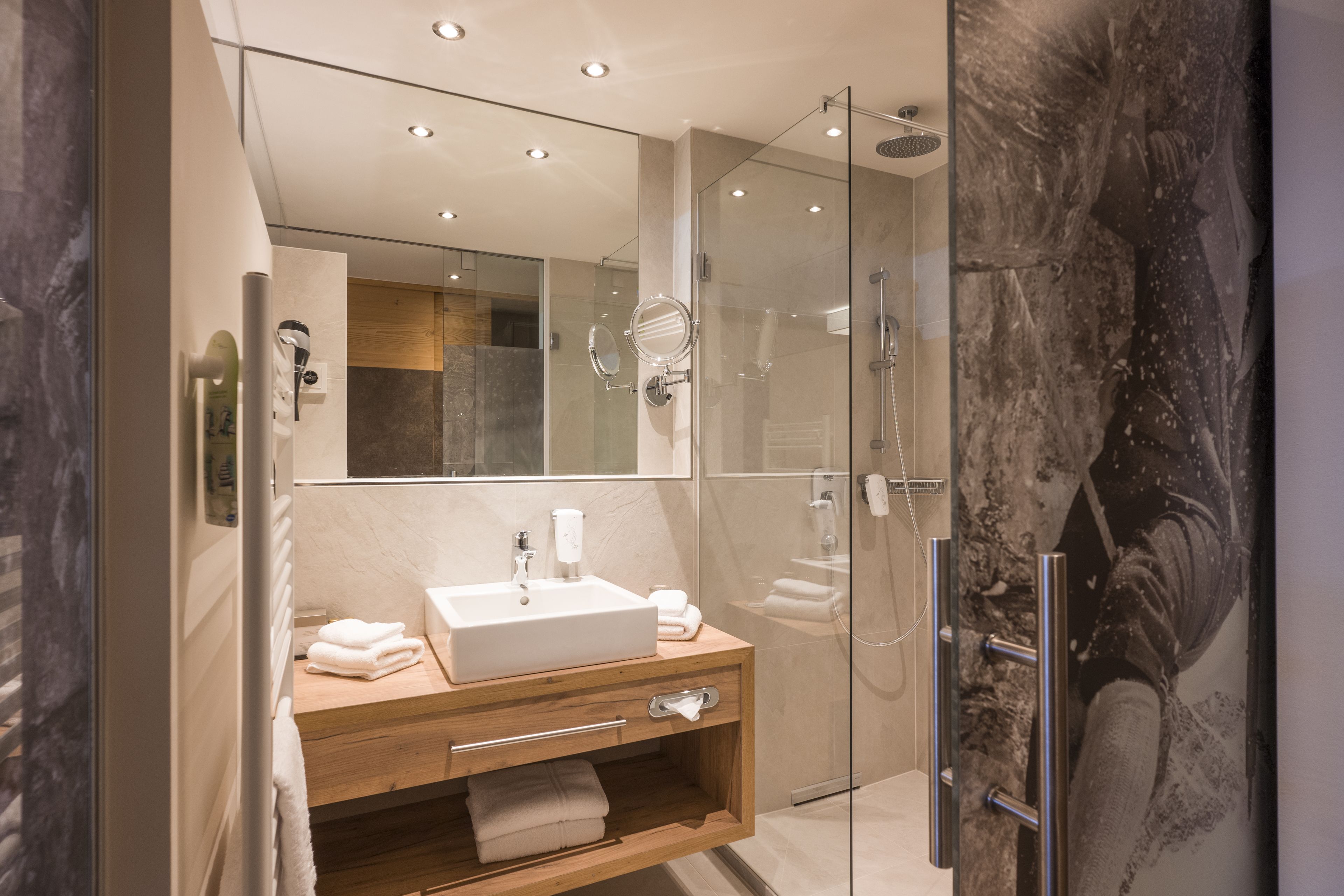 A modern bathroom with a glass-enclosed shower, a wooden vanity with a sink, and a large mirror.