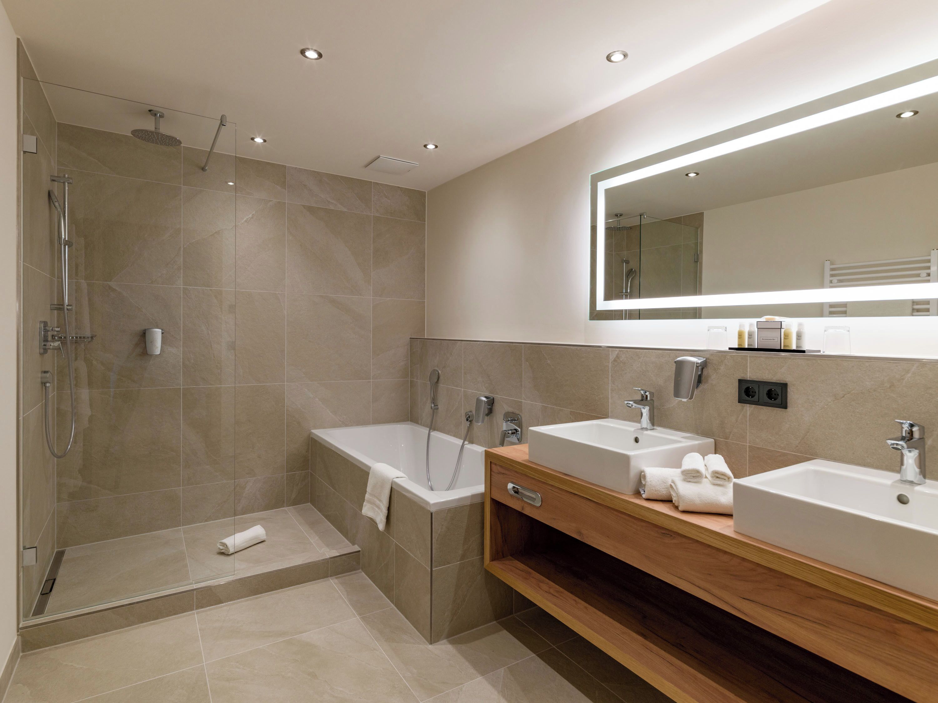 A modern bathroom with a glass-enclosed shower, two sinks, a mirror, and a wooden vanity.