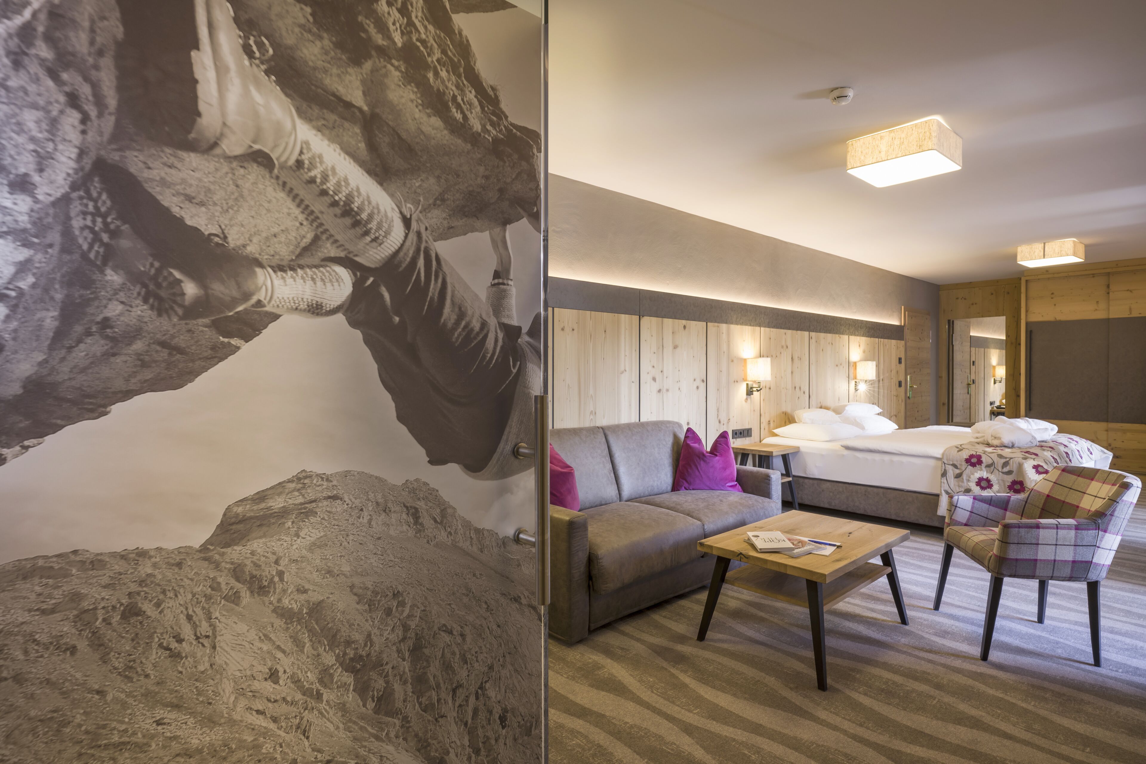 A hotel room with a bed, a sofa, a chair, a table, and a wall with a textured mural.