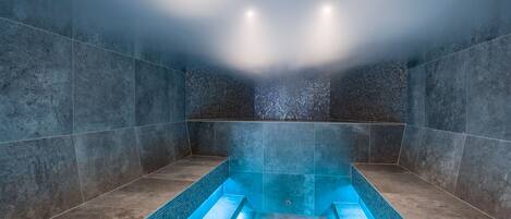 A modern spa room with a large, rectangular hot tub and tiled walls.