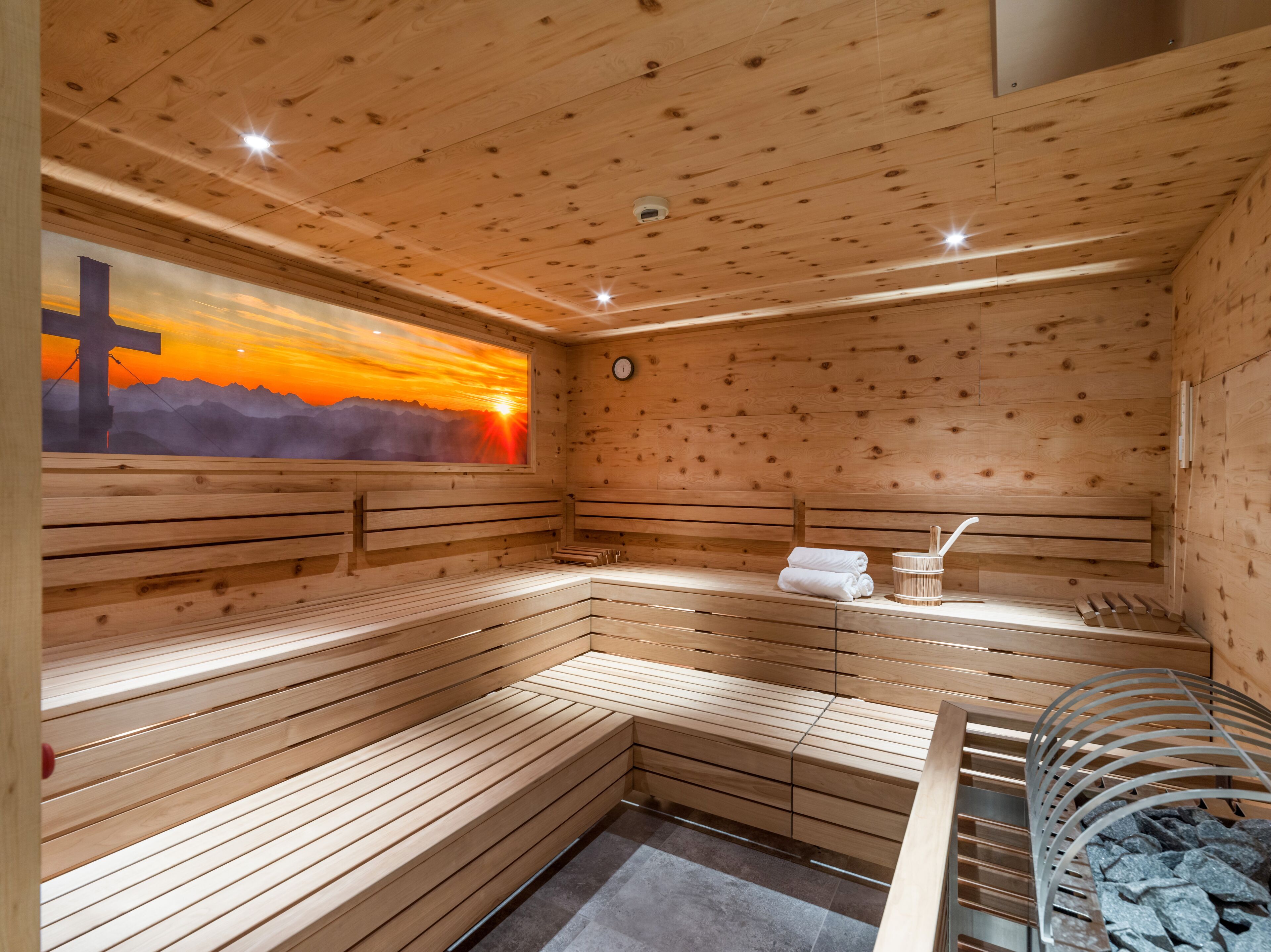 Eine Holzsauna mit Bänken, einer Wanduhr und einem Fenster mit Sonnenuntergangsblick.