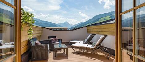 A sunlit outdoor patio with wicker furniture, a table, and a view of mountains.