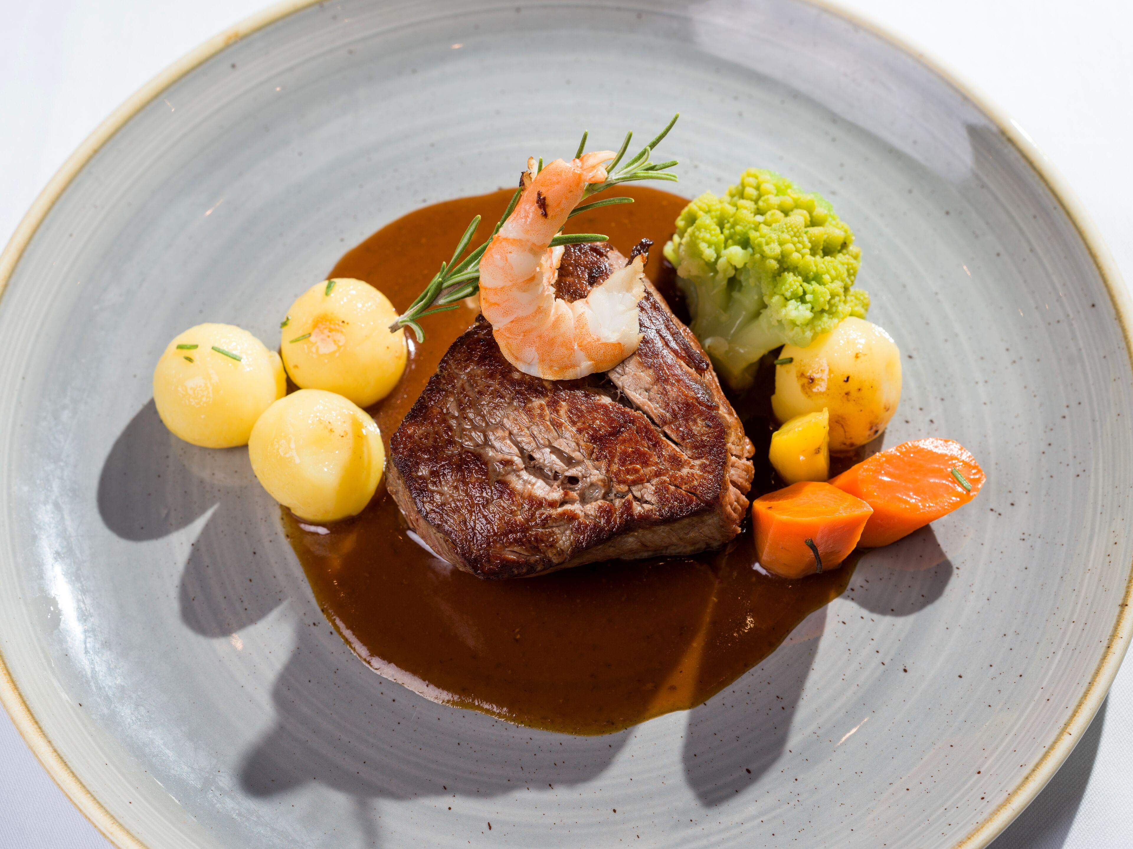 Une assiette contenant un steak, des crevettes, des pommes de terre, des carottes et des brocolis.