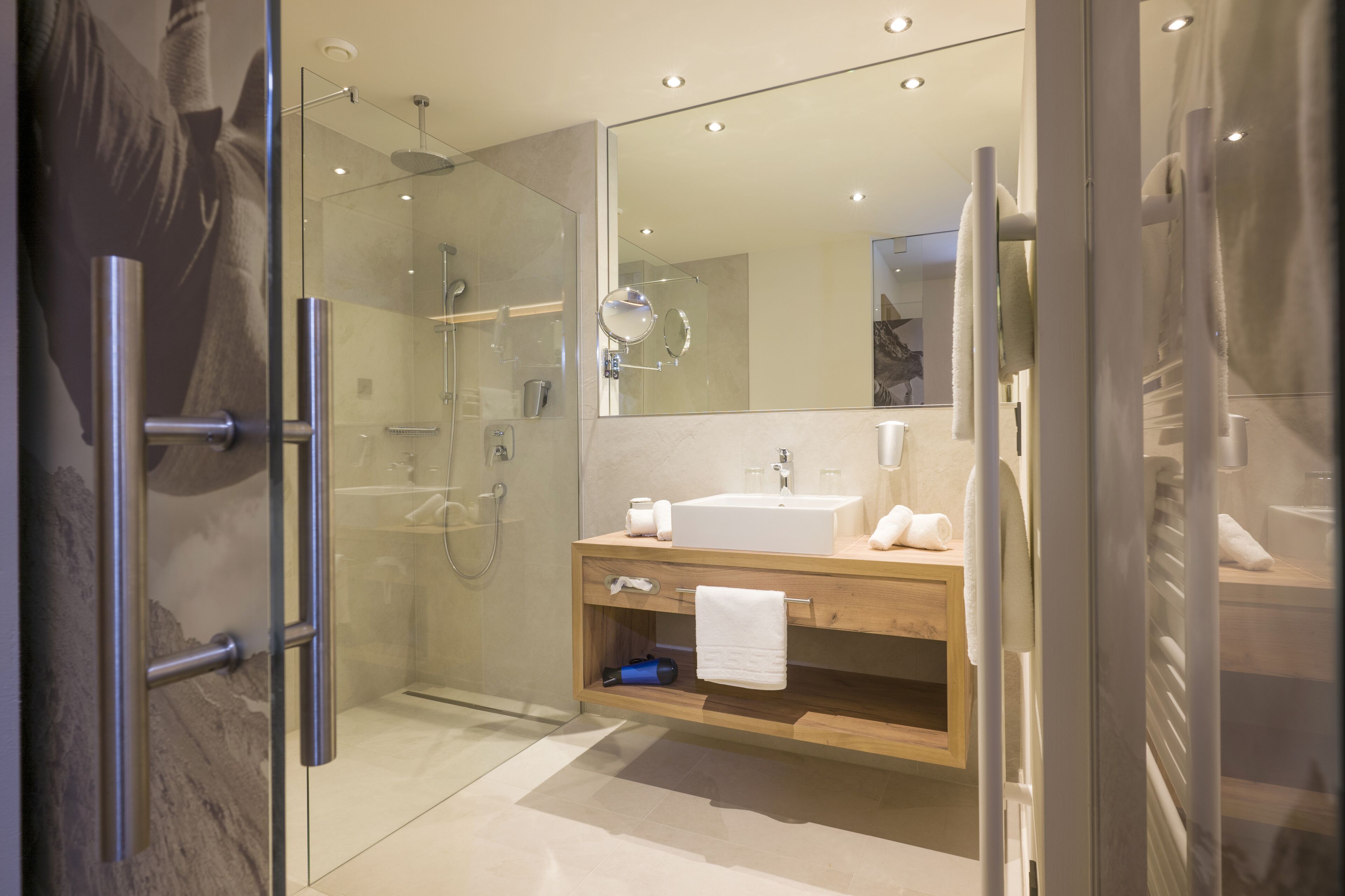A modern bathroom with a glass-enclosed shower, a wooden vanity with a sink, and a large mirror.